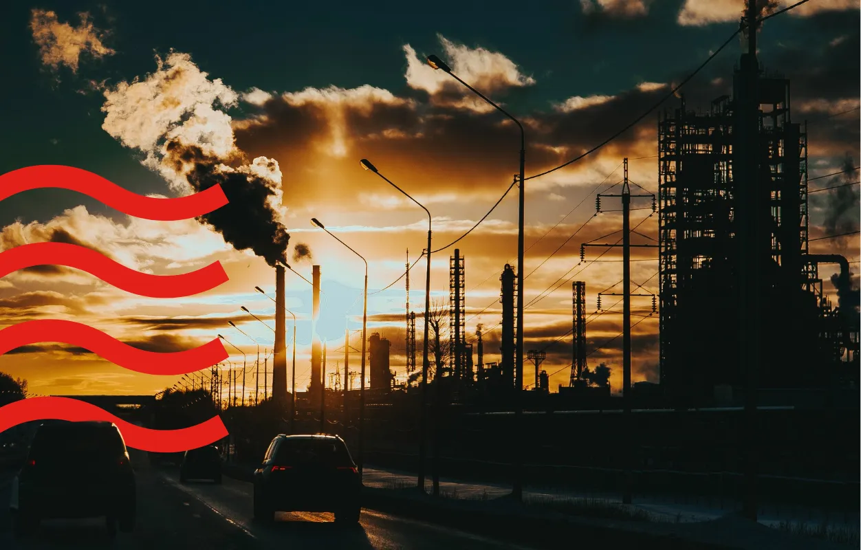 Cars driving past industrial chimneys emitting smoke at sunset