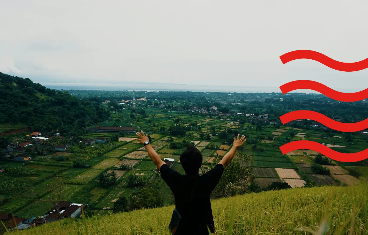 Person standing on a hillside with arms raised, overlooking a green valley
